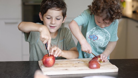 Gesunde Zwischenmahlzeit: Zwei Kinder schneiden sich Äpfel zurecht.