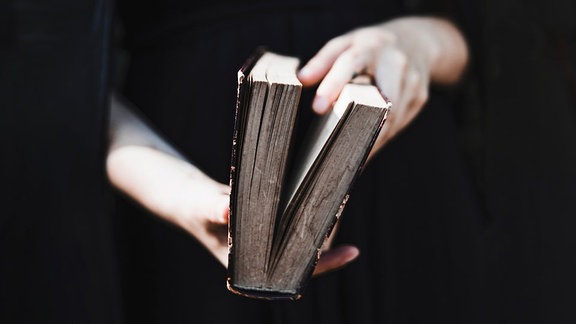 Eine Person mit Umhang hält ein magisches Buch in der Hand.