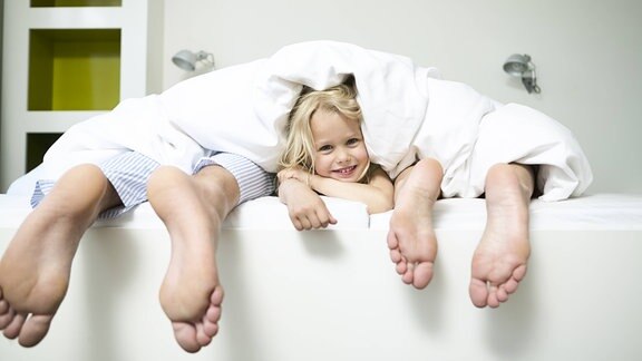 Familie im Bett - die Tochter schaut zwischen den Füßen der Eltern hervor