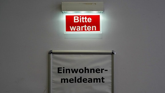 Der Schriftzug "Bitte warten" steht über dem Schild des Behördenbereichs Einwohnermeldeamt in Markkleeberg in Sachsen.