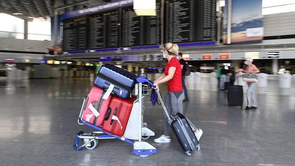 Urlauberin mit einem voll beladenen Gepäckwagen und Maske auf dem Frankfurter Flughafen