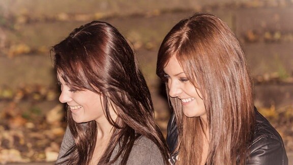Zwei junge Frauen mit dunklen Haaren lächeln, sehen sich sehr ähnlich