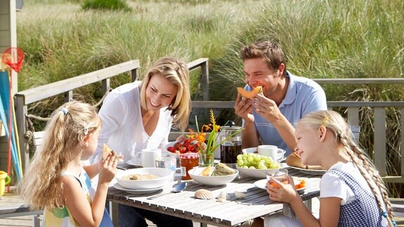 Eine Familie frühstückt im Sommer bei Sonne im Freien (Symbolbild)