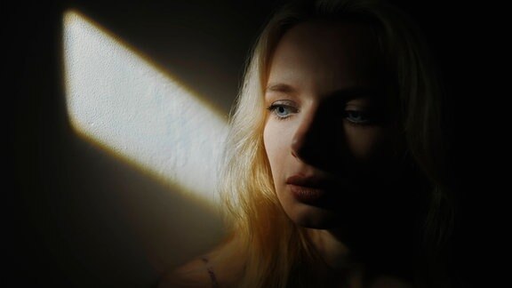 Frau sitzt an einer Wand und wird von Sonnenstrahlen beleuchtet (Symbolfoto)