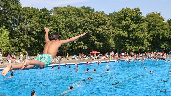 Ein Junge springt im Freibad vom Sprungbrett