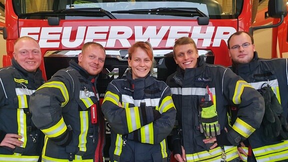 Fünf Feuerwehrleute der Freiwilligen Feuerwehr in Calbe Saale stehen vor einem Feuerwehrwagen