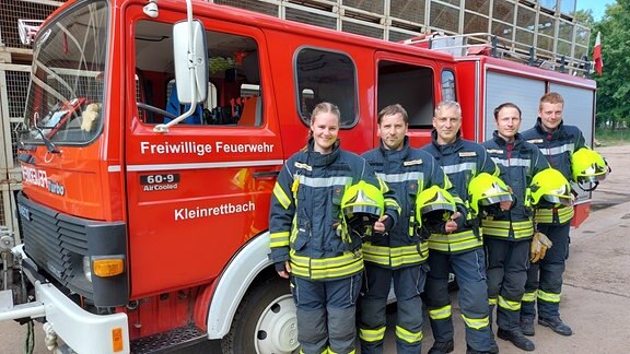 Fünf Feuerwehrleute der Freiwilligen Feuerwehr in Kleinrettbach stehen vor einem Feuerwehrwagen