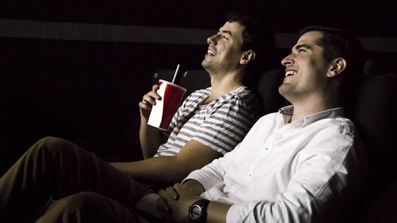 Zwei Freunde sitzen im Kino und schauen einen lustigen Film. Sie lachen.