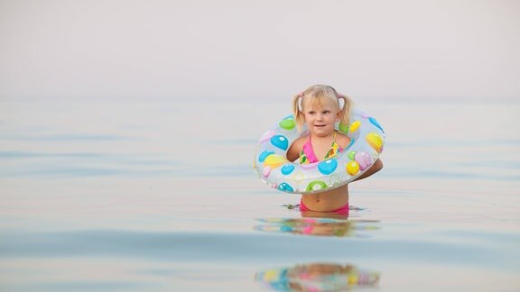 Kleines Mädchen mit Schwimmring im flachen Wasser