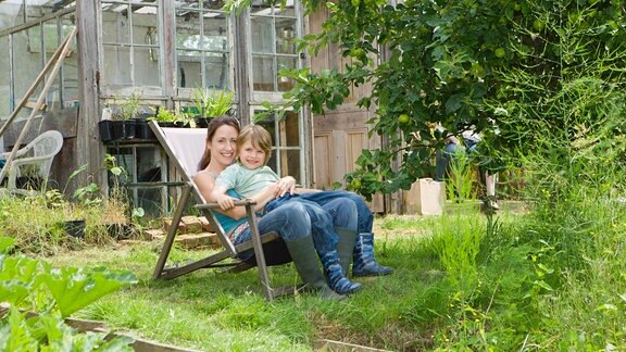 Zum Ausruhen und Wohlfühlen: Mutter und Sohn auf einem Stuhl einem grünen Garten (Symbolbild)