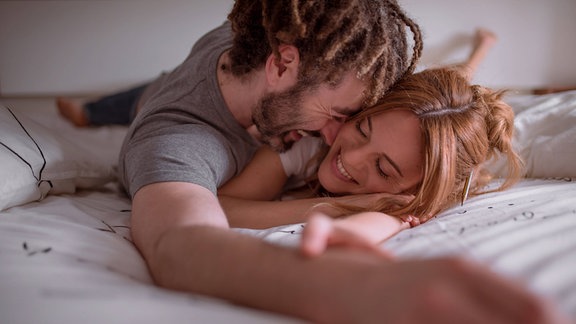 Mann und Frau, die sich umarmen und küssen, während sie zusammen auf dem Bauch auf dem Bett liegen