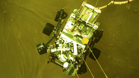 Der Mars Rover Perseverance von oben, aus der Perspektive des Landemoduls. Er schwebt über der Marsoberfläche.