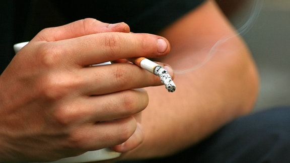Auf dem Bild ist eine Hand zu sehen. Zwischen den beiden Finger steckt eine qualmende Zigarette.
