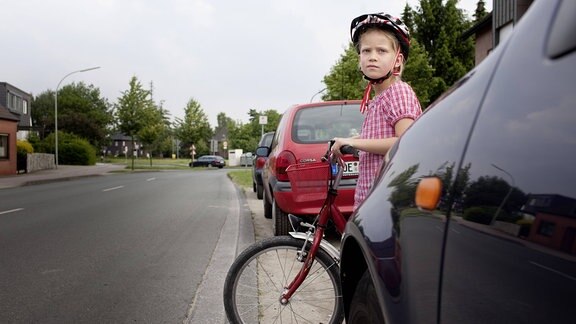 Ein Schulkind mit Fahrrad ist hinter einem Auto eher schwer zu sehen.