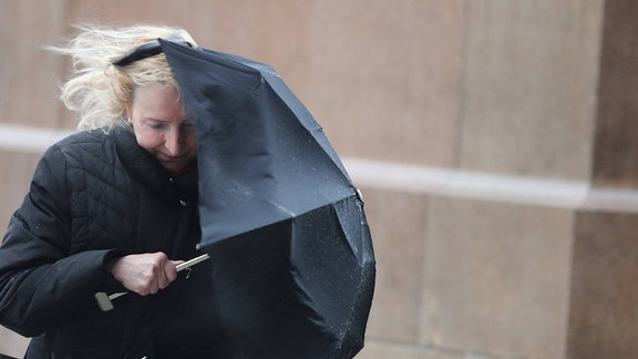 Eine Frau mit Regenschirm kämpft mit dem Gegenwind.