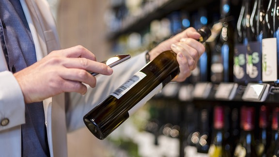 Ein Mann scannt mit seinem Smartphone einen Wein im Supermarkt