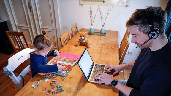 Er arbeitet, sie puzzelt: Vater und Tochter im Homeoffice in Berlin